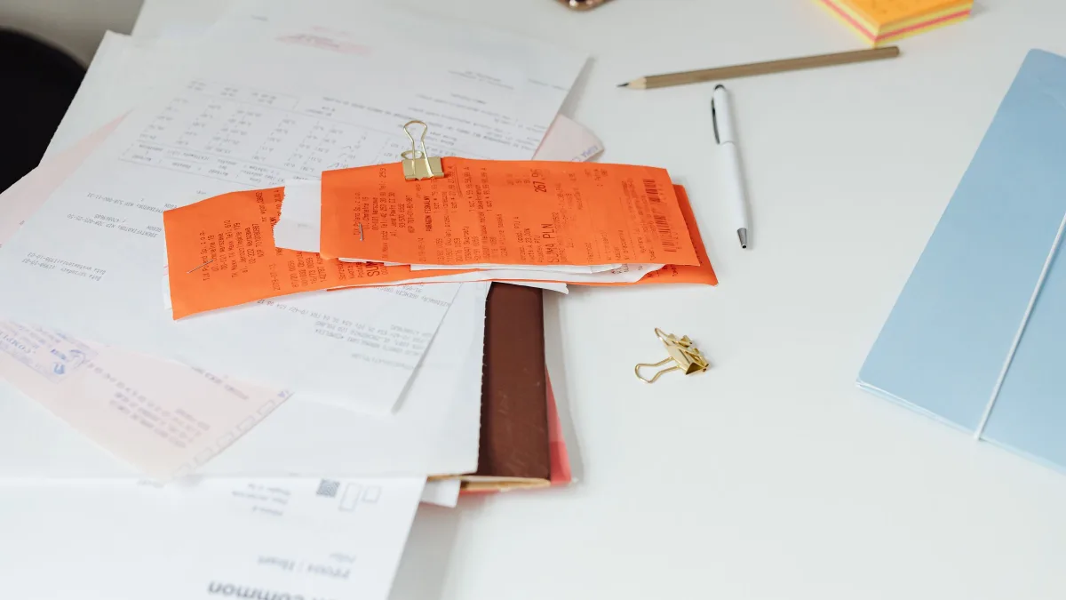 Recibos y documentos en papel esparcidos sobre una mesa de trabajo junto a un bolígrafo