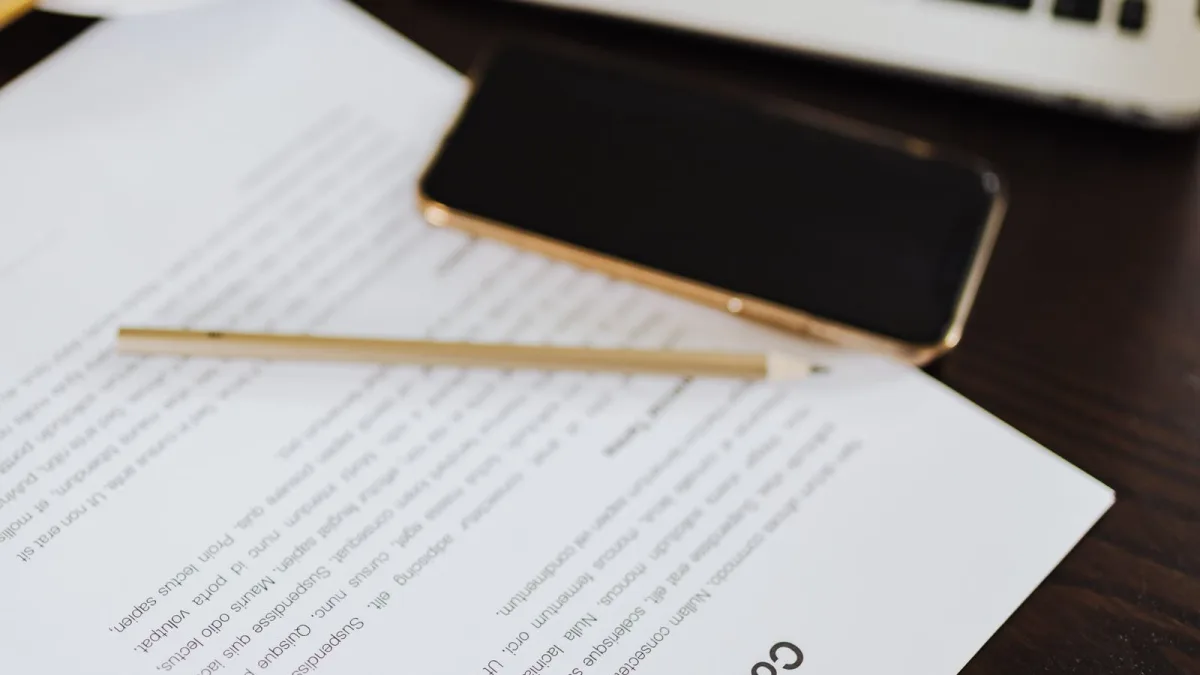 Un contrato en papel sobre un escritorio junto a un portátil y un móvil