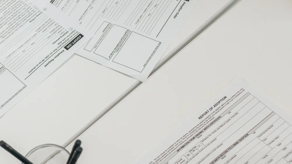Dos documentos impresos con formularios y tablas, uno sobre otro, en una mesa blanca junto a un bolígrafo