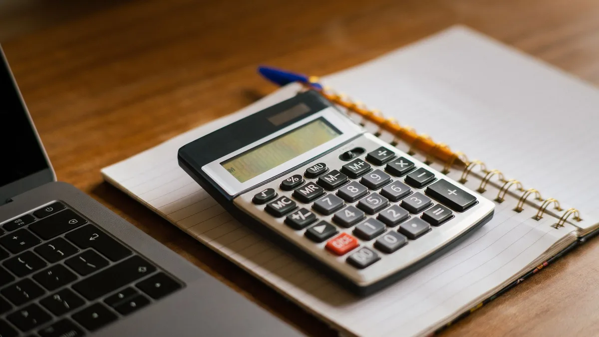 Calculadora y cuaderno de anillas sobre un portátil, en una mesa de madera