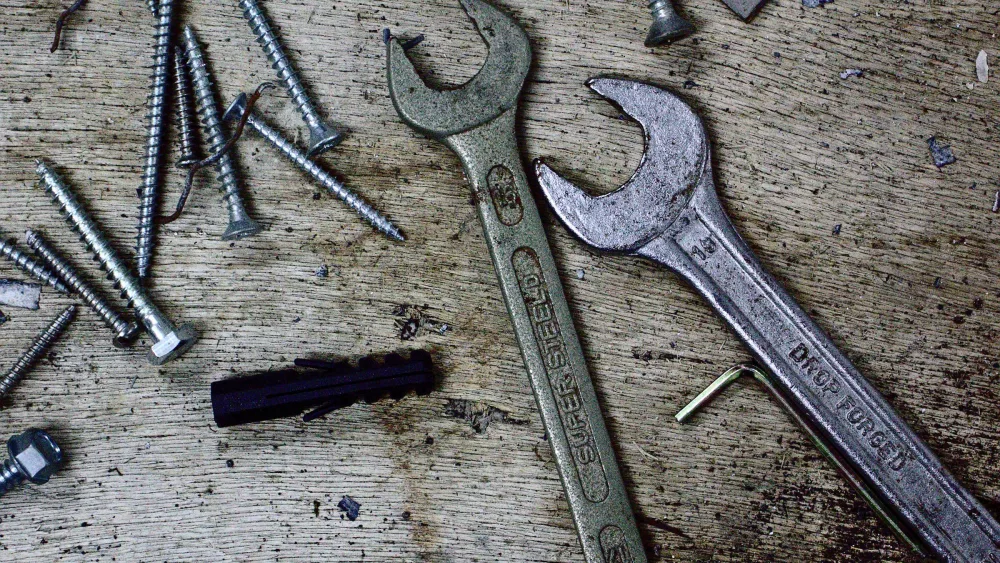 Una llave inglesa y una llave fija junto a tornillos de distintos tamaños sobre un banco de madera