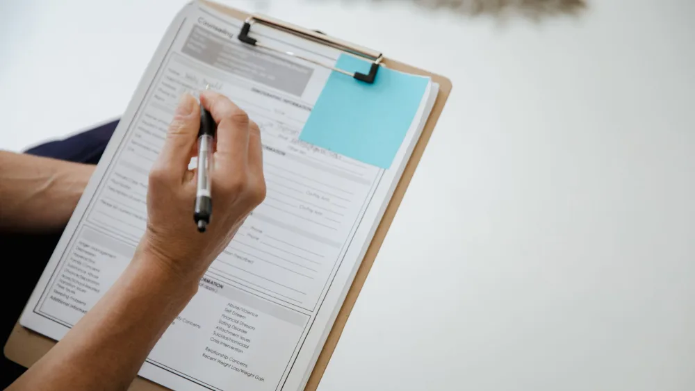 Una persona rellena a mano un formulario sujeto a una carpeta con pinza