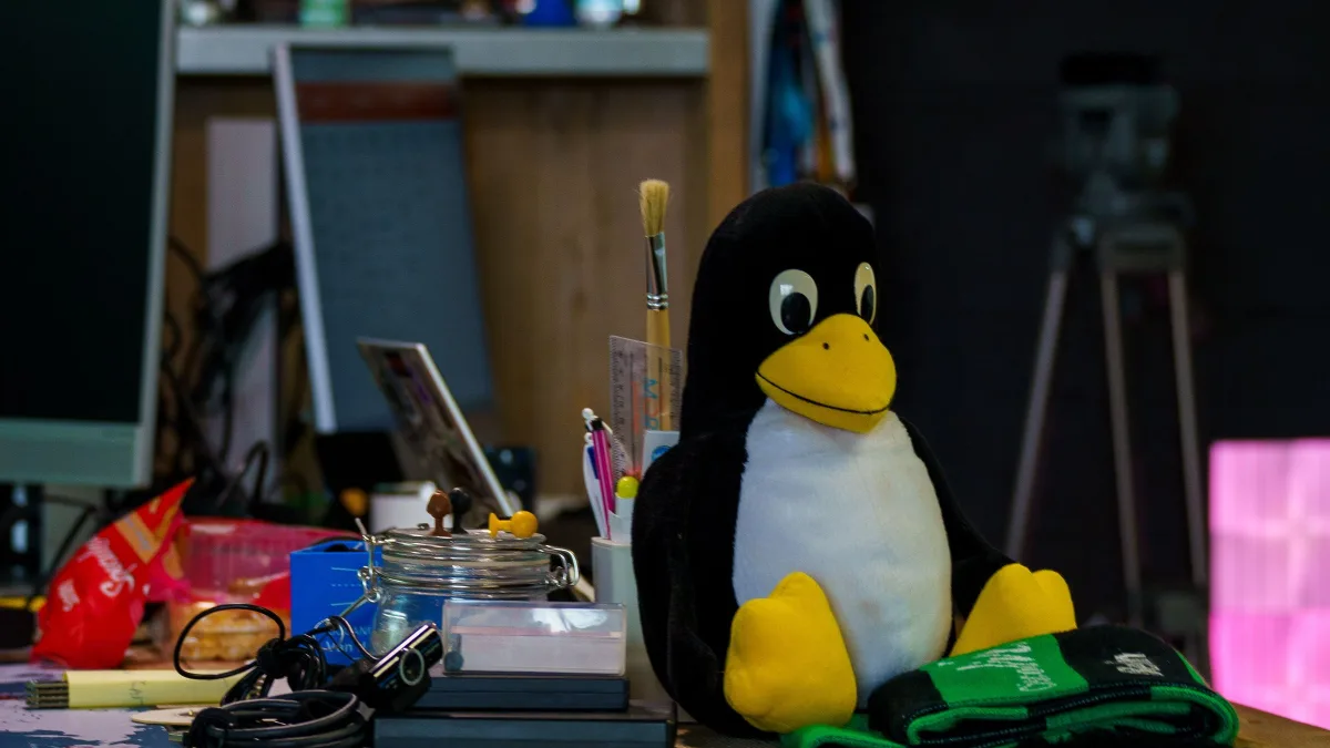 Un peluche del pingüino Tux sobre una mesa de trabajo llena de cacharros