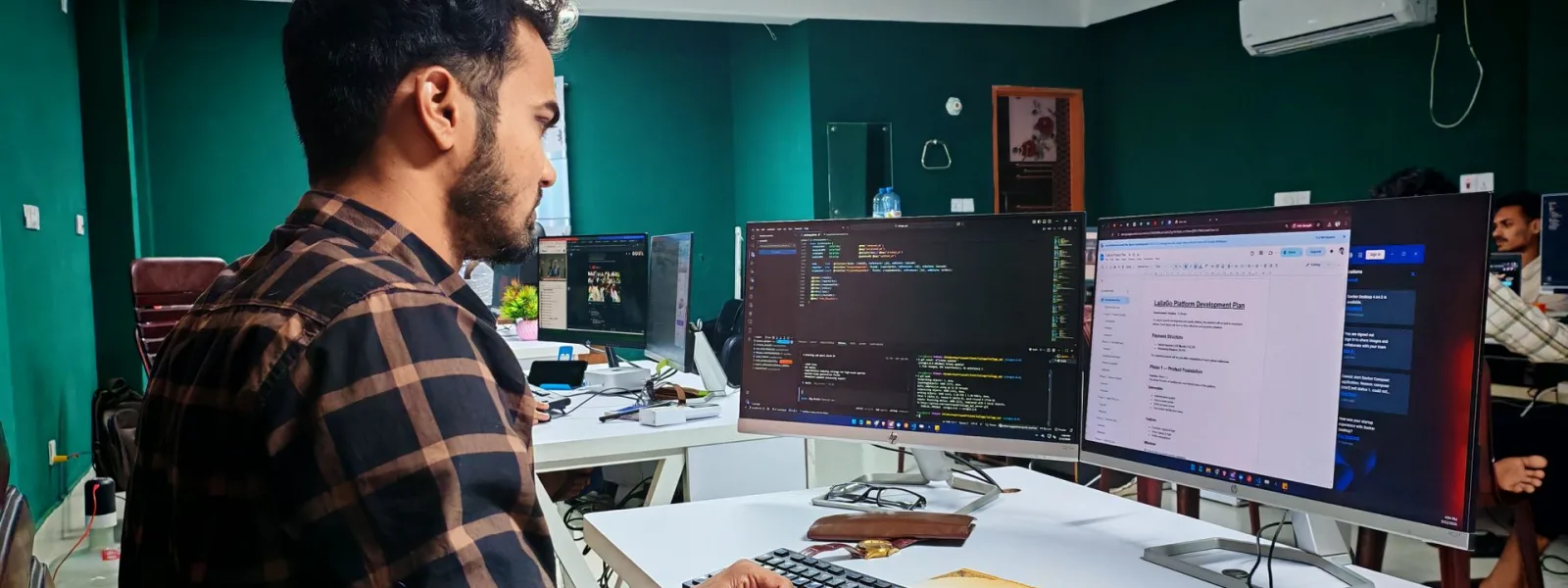 Desarrollador trabajando en código a doble pantalla, con el plan de un proyecto de software en marcha